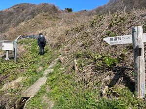 展望台への立て看板があり、遠くまで見渡せる山肌に道が続く写真