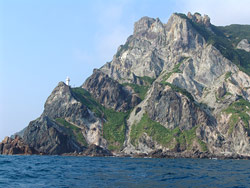 海の先に、ごつごつと切り立った岩肌に所々緑がある島の景色の写真