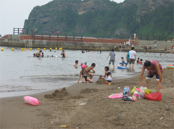 浅瀬で泳いで遊ぶ子供たちと、見守る大人の写真