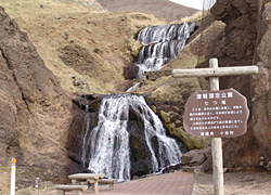 山岳の岩肌から、七段になった滝の水が勢いよく流れ落ちてくる風景の七つ滝の写真