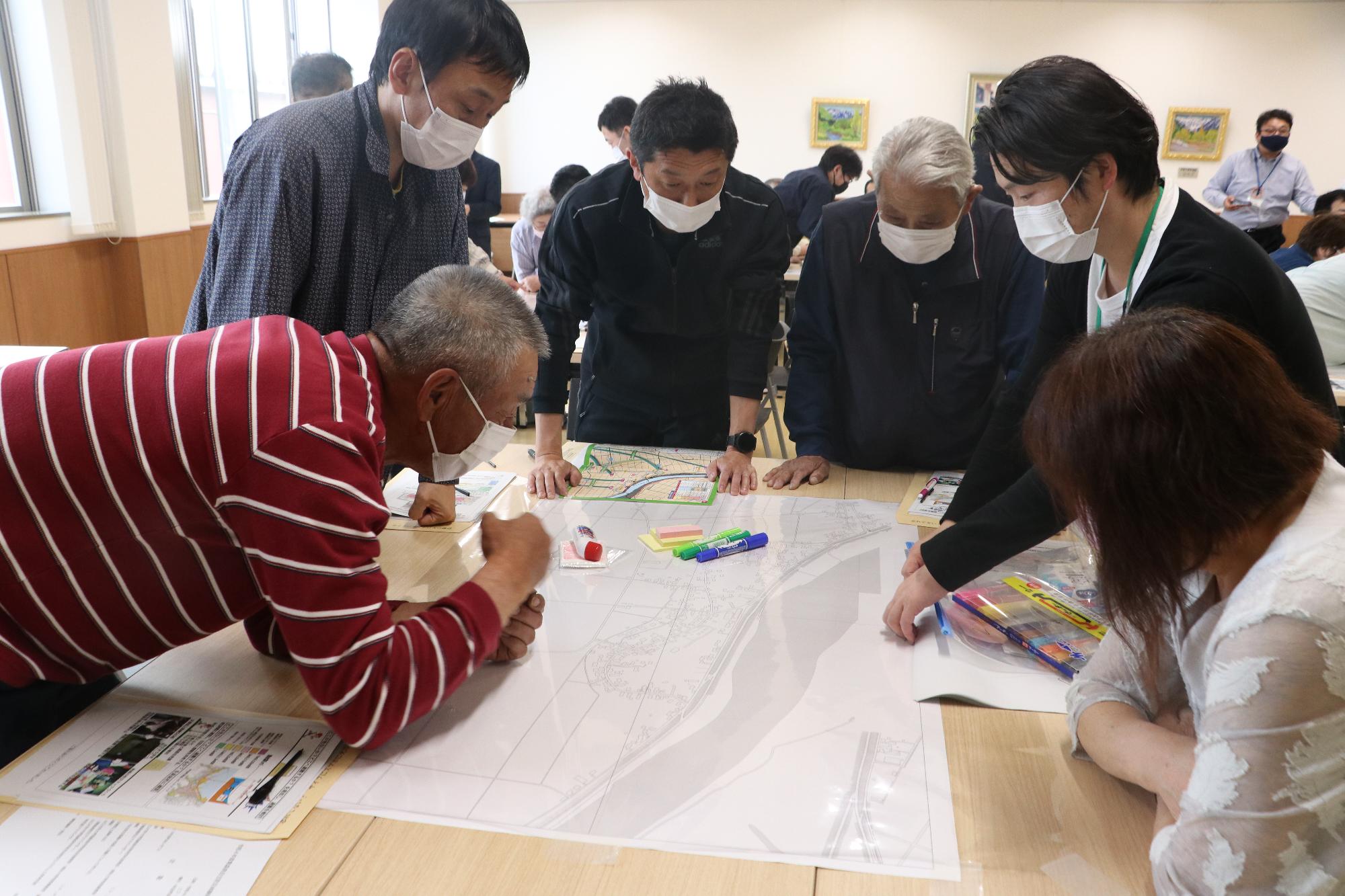 6人の大人が机の上に広げた地図を囲み、話し合いをしている写真