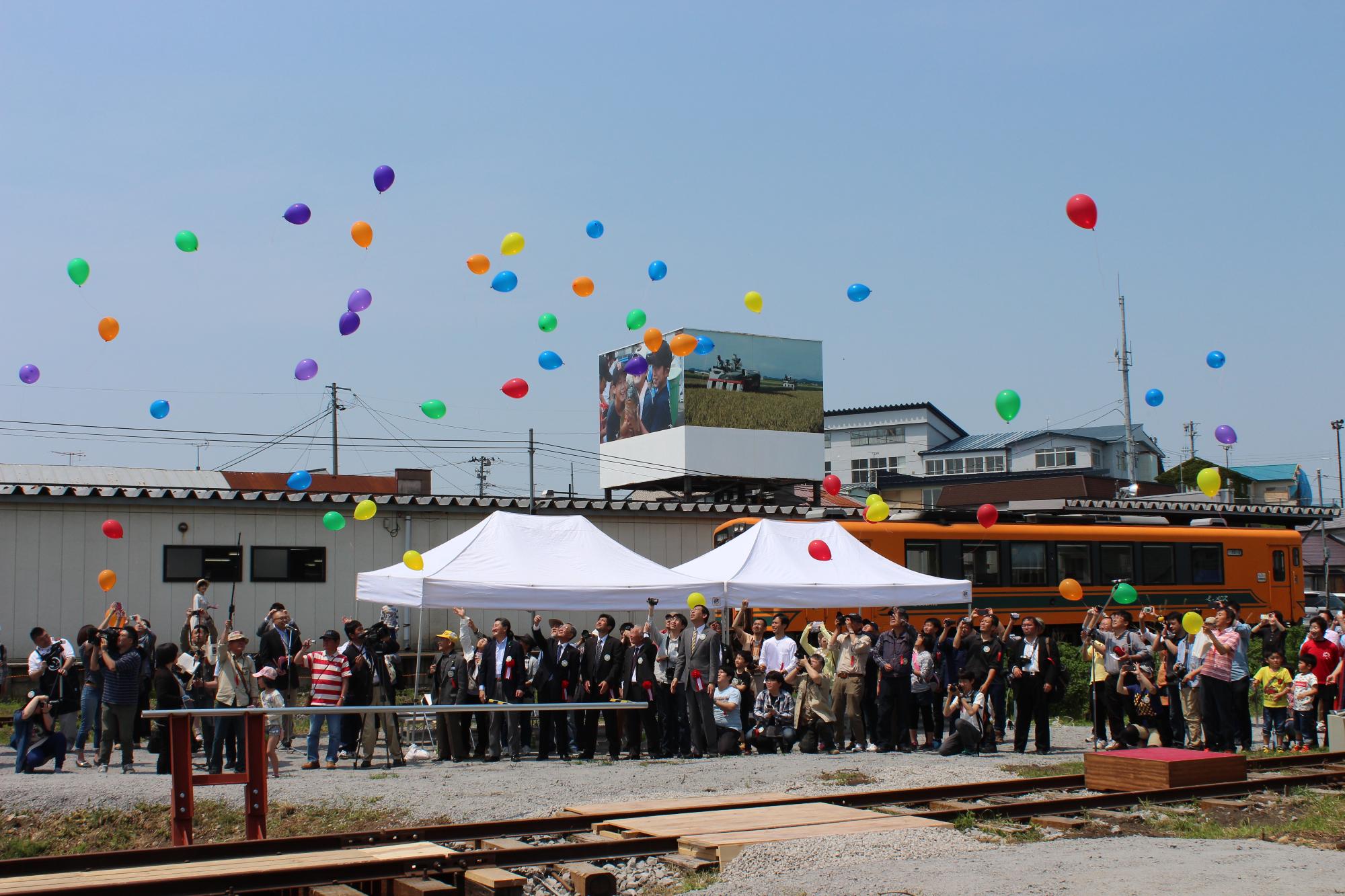 津軽中里駅に大勢の人が集まり、色とりどりの風船が空に舞い上がっている写真