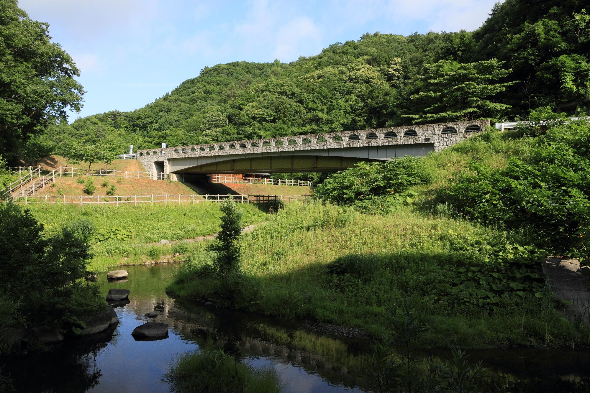 丘に石橋がかけられ、その下を小川が流れている写真